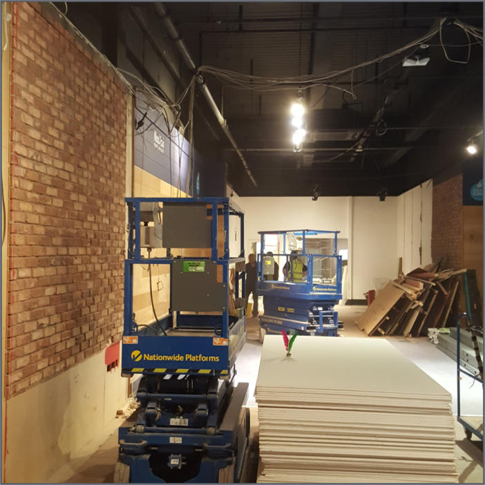 Shop fit-out in progress, showing exposed brickwork, ceiling installation and access equipment